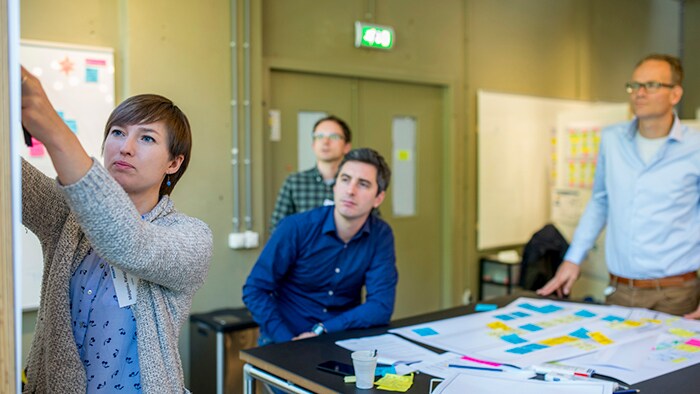 A woman in a conference room adds something to a whiteboard while coworkers look on