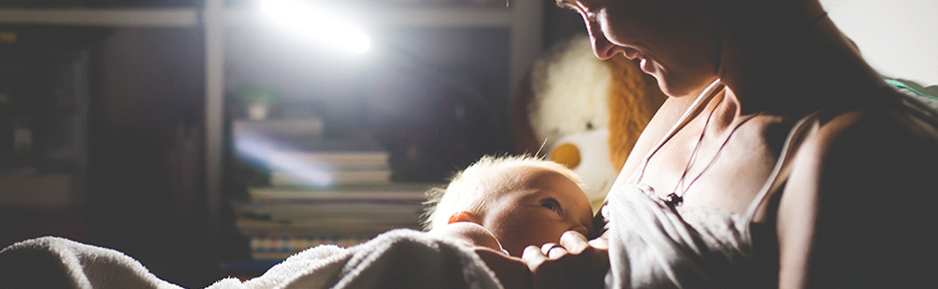 A baby sucking on their mom's breast in dim lighting